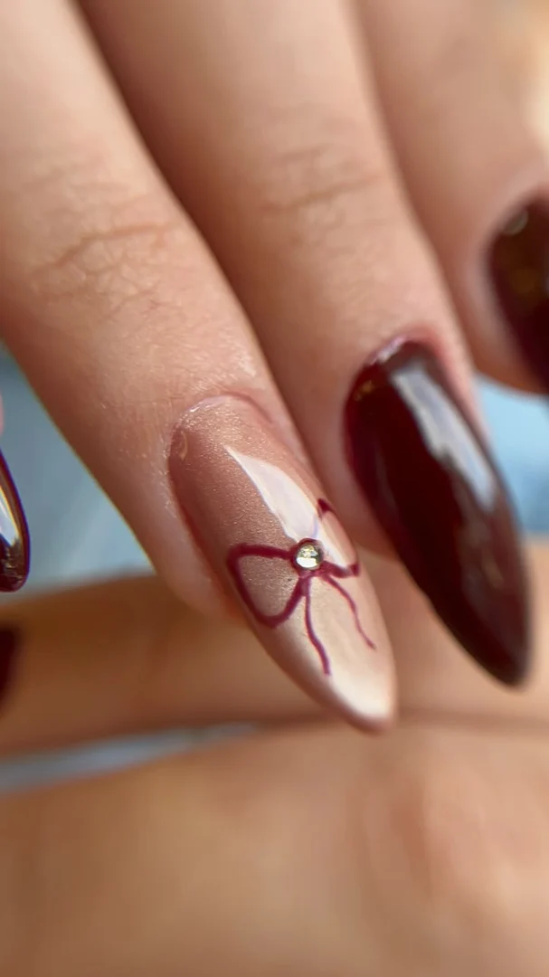 Unhas amendoadas, uma nude com laço desenhado e outra vinho, trabalho da Terumi Nails