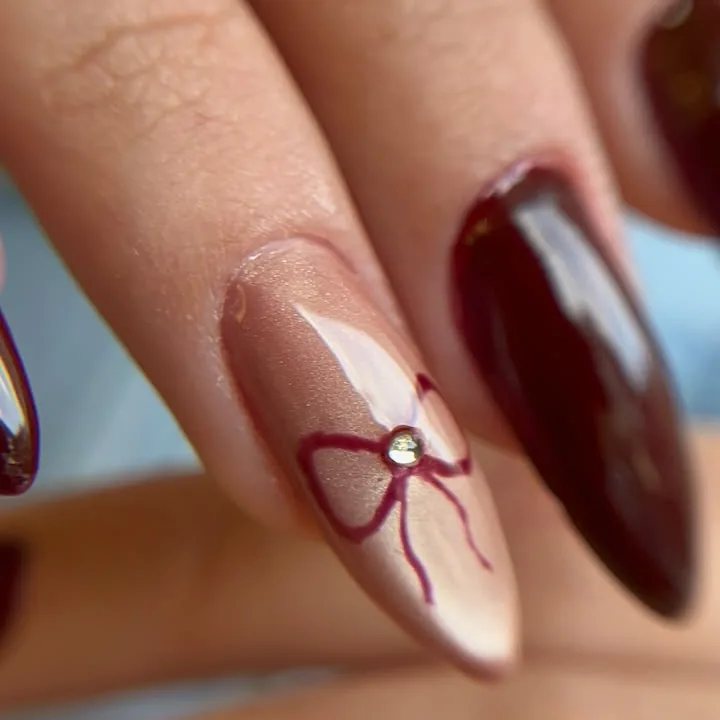 Nail art com laço em tom vinho sobre base nude