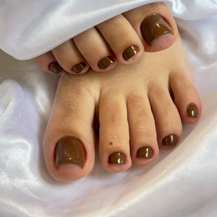 Pedicure com esmaltação em gel marrom sobre tecido branco